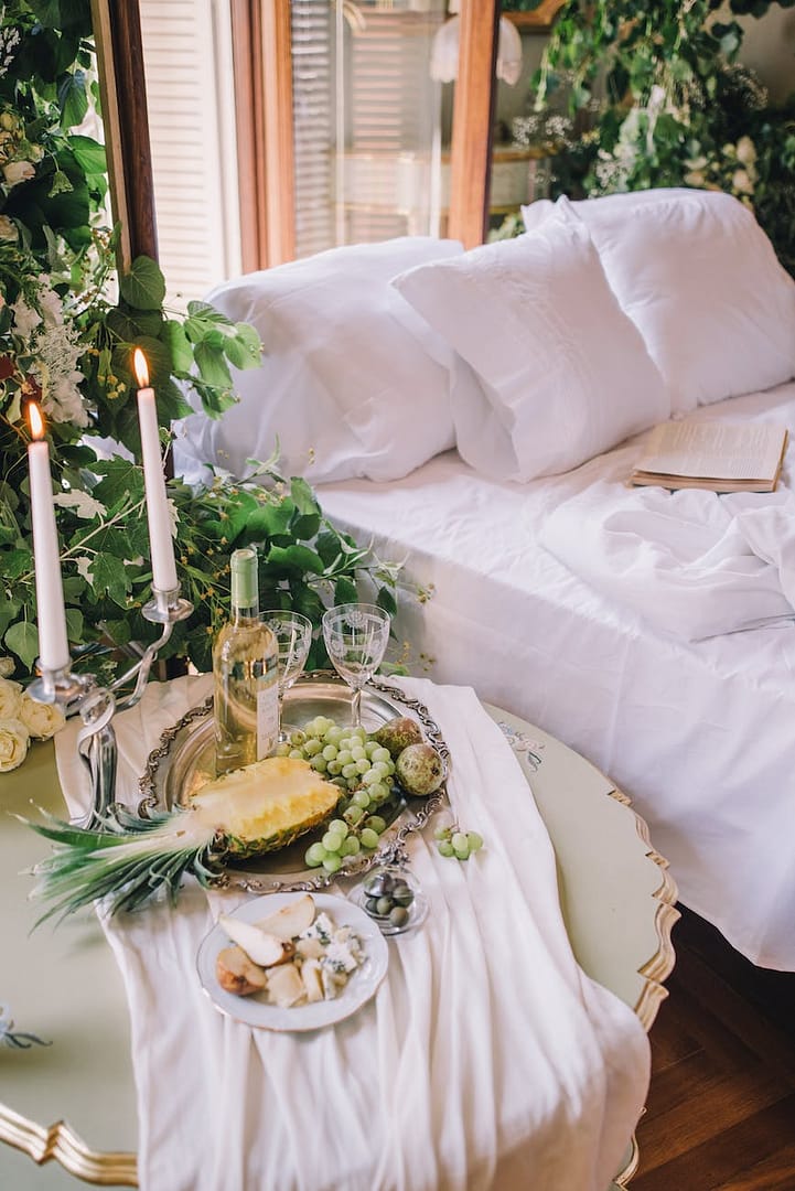 elegant table with a tray of fruit white wine and a candlestick by the bed